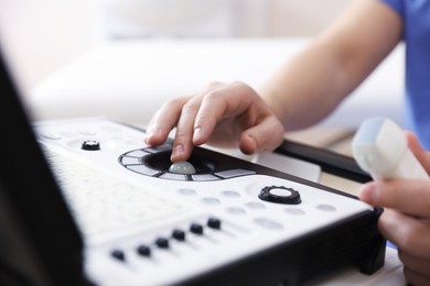Photo of Sonographer with transducer and ultrasound machine in clinic, closeup