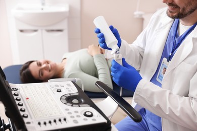 Photo of Sonographer applying gel on ultrasound transducer and woman waiting for examination in clinic, selective focus