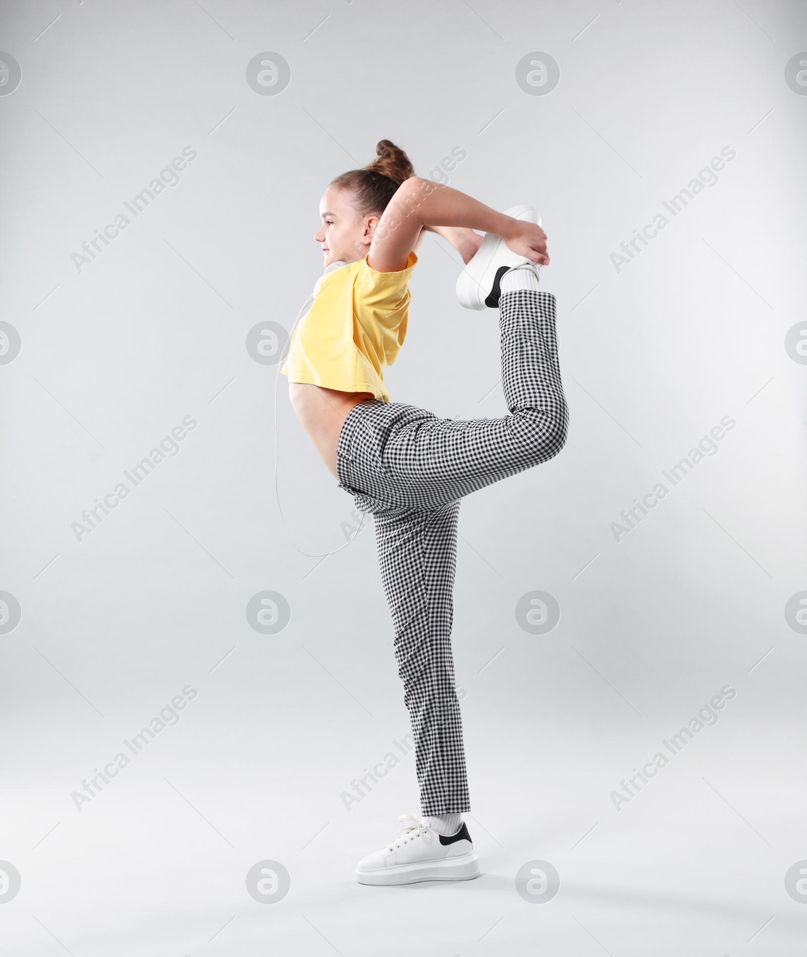 Girl with headphones in stylish clothes dancing on light grey background Photo of Girl with headphones in stylish clothes dancing on light grey background