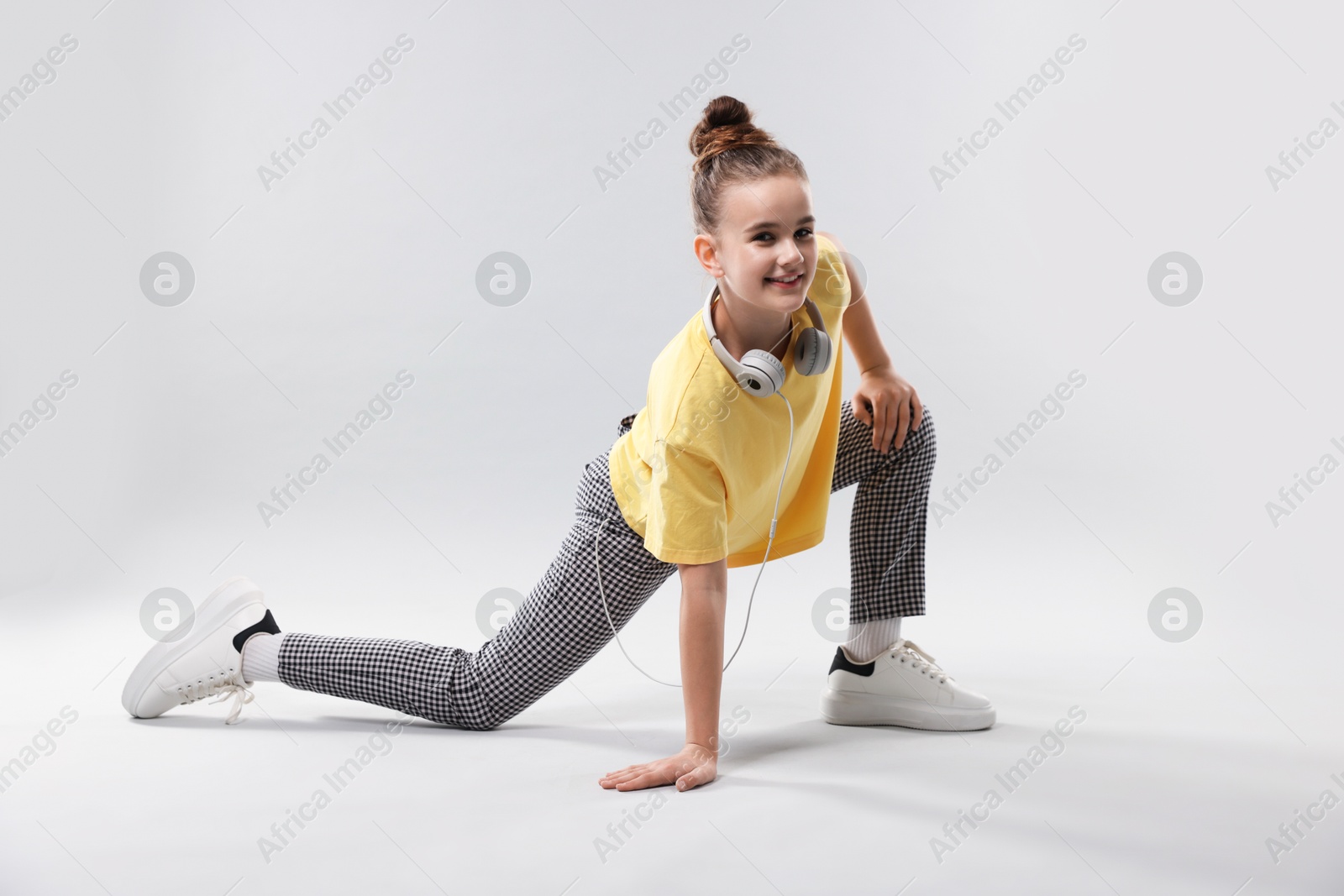 Girl with headphones in stylish clothes dancing on light grey background Photo of Girl with headphones in stylish clothes dancing on light grey background