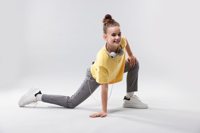 Photo of Girl with headphones in stylish clothes dancing on light grey background