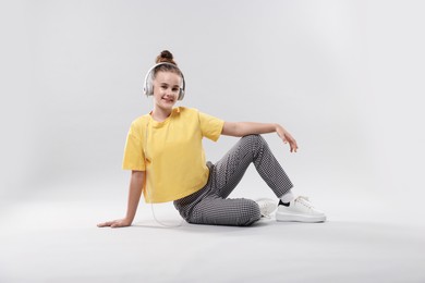 Photo of Girl with headphones in stylish clothes dancing on light grey background
