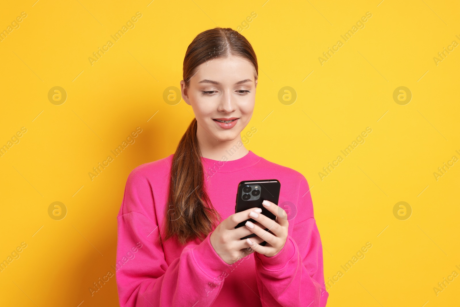 Teenage girl with smartphone on yellow background Photo of Teenage girl with smartphone on yellow background