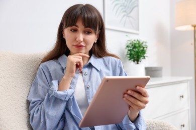 Photo of Woman using modern tablet in armchair at home