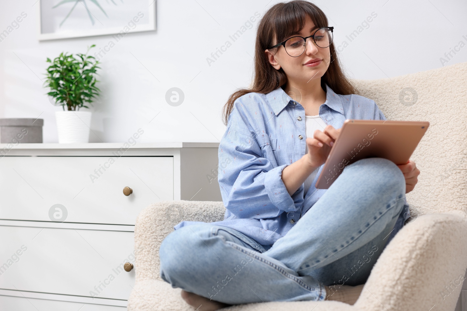 Woman using modern tablet in armchair at home. Space for text Photo of Woman using modern tablet in armchair at home. Space for text