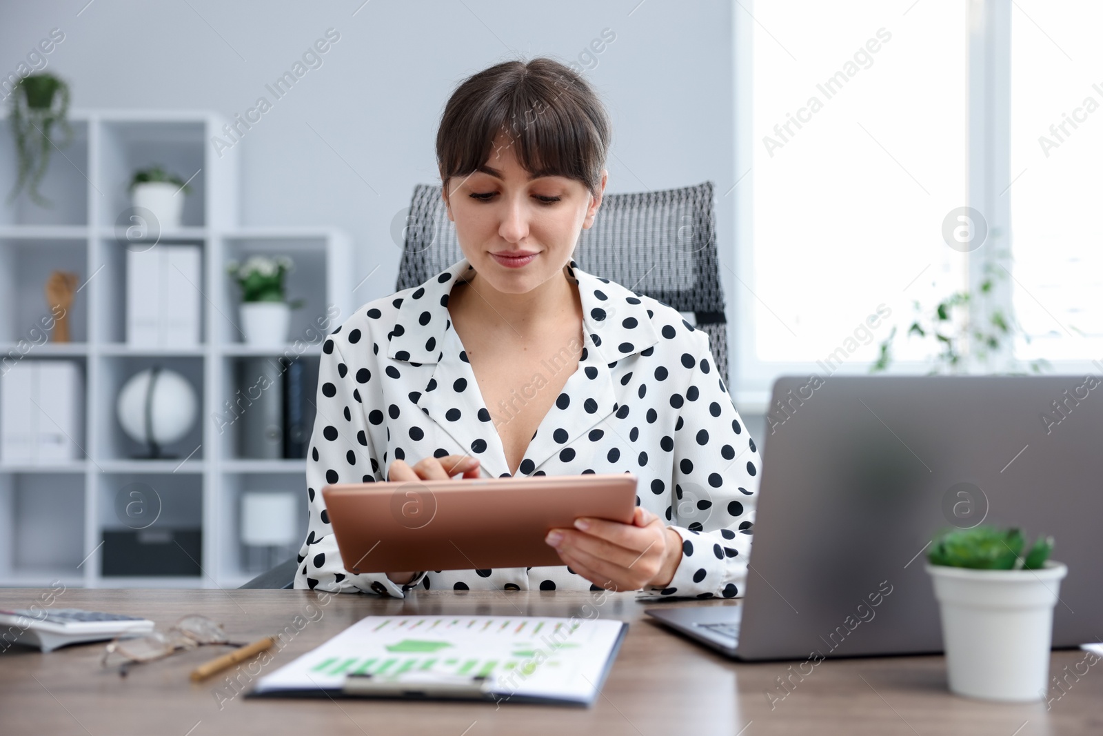 Woman using modern tablet at desk in office Photo of Woman using modern tablet at desk in office