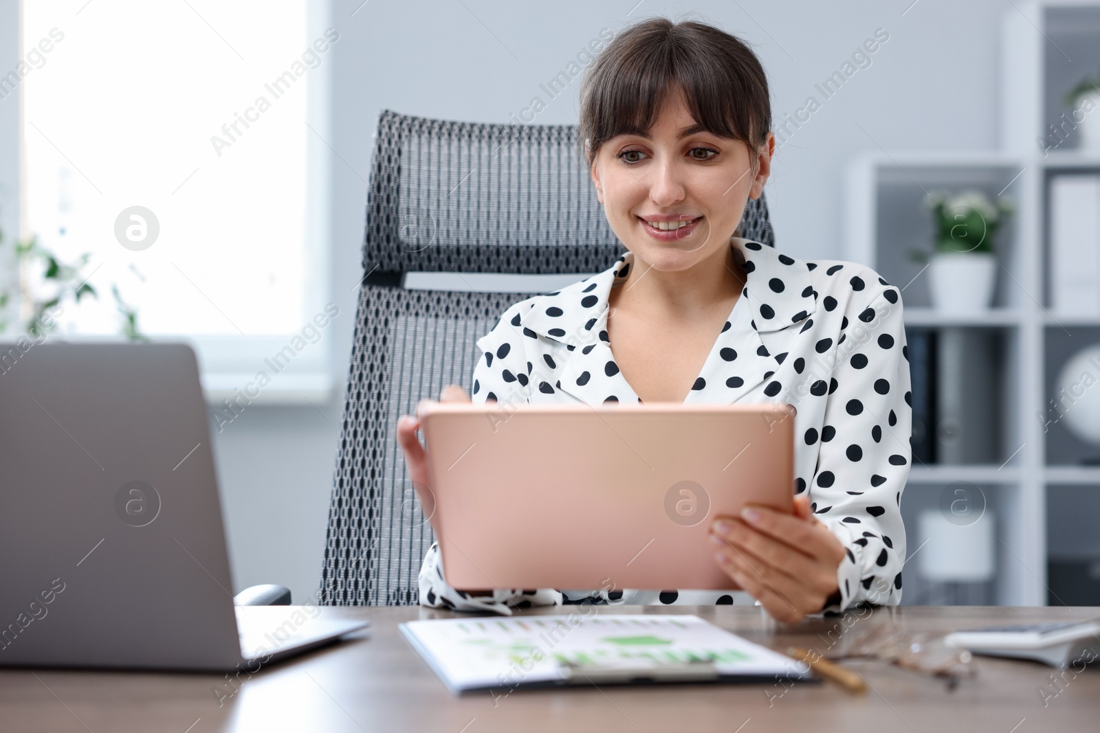 Woman using modern tablet at desk in office Photo of Woman using modern tablet at desk in office