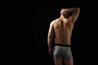 Photo of Young man in stylish light grey underwear on black background, back view. Space for text