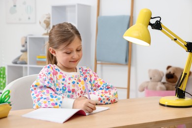 Photo of Little girl doing homework at table indoors
