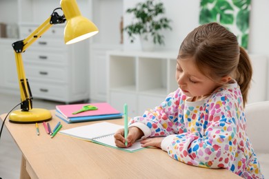 Photo of Little girl doing homework at table indoors