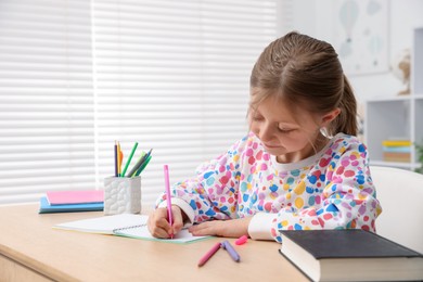 Photo of Little girl doing homework at table indoors