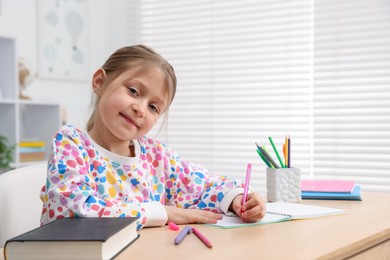 Photo of Little girl doing homework at table indoors