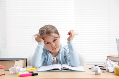 Photo of Tired little girl doing homework at table indoors