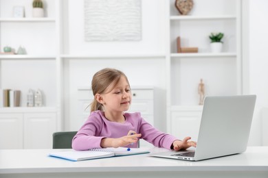 Photo of Little girl doing homework at table indoors
