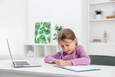Photo of Little girl doing homework at table indoors
