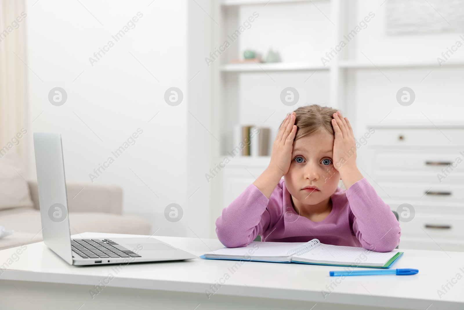 Tired little girl doing homework at table indoors Photo of Tired little girl doing homework at table indoors