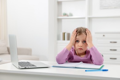 Photo of Tired little girl doing homework at table indoors