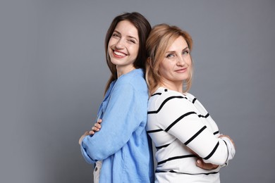 Photo of Cheerful mother and daughter back to back on grey background
