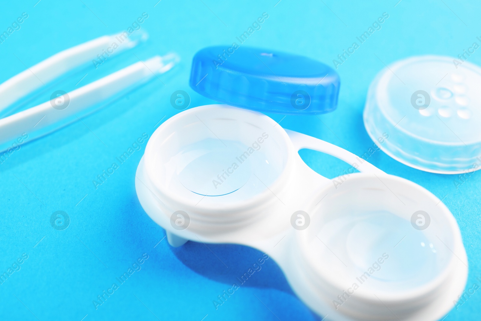 Contact lenses in case and tweezers on light blue background, closeup Photo of Contact lenses in case and tweezers on light blue background, closeup