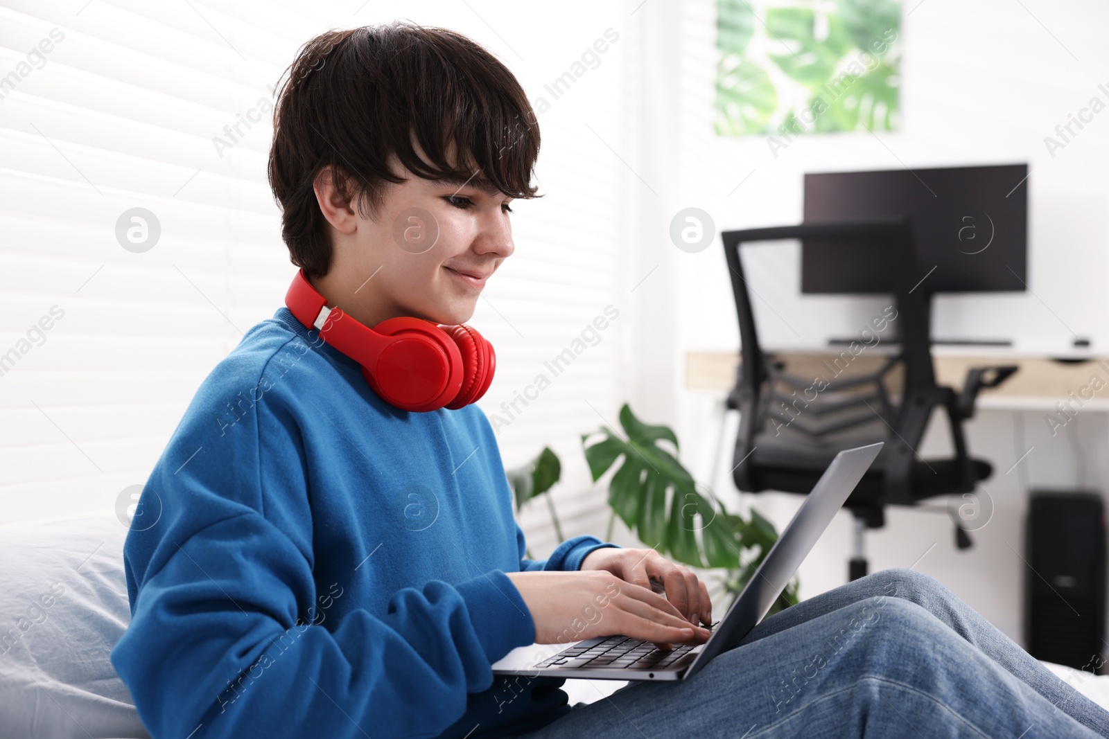 Teenage boy with headphones and laptop on bed at home Photo of Teenage boy with headphones and laptop on bed at home