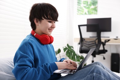 Photo of Teenage boy with headphones and laptop on bed at home