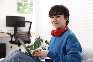 Photo of Teenage boy with headphones and laptop on bed at home