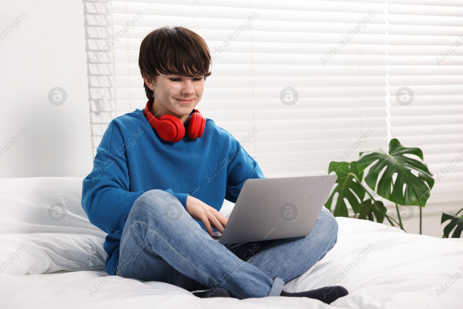 Teenage boy with headphones and laptop on bed at home Photo of Teenage boy with headphones and laptop on bed at home