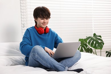 Photo of Teenage boy with headphones and laptop on bed at home