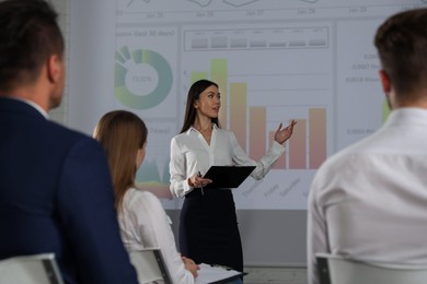Photo of Female business trainer giving lecture in conference room with projection screen