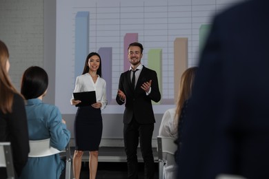 Photo of Business trainers giving lecture in conference room with projection screen