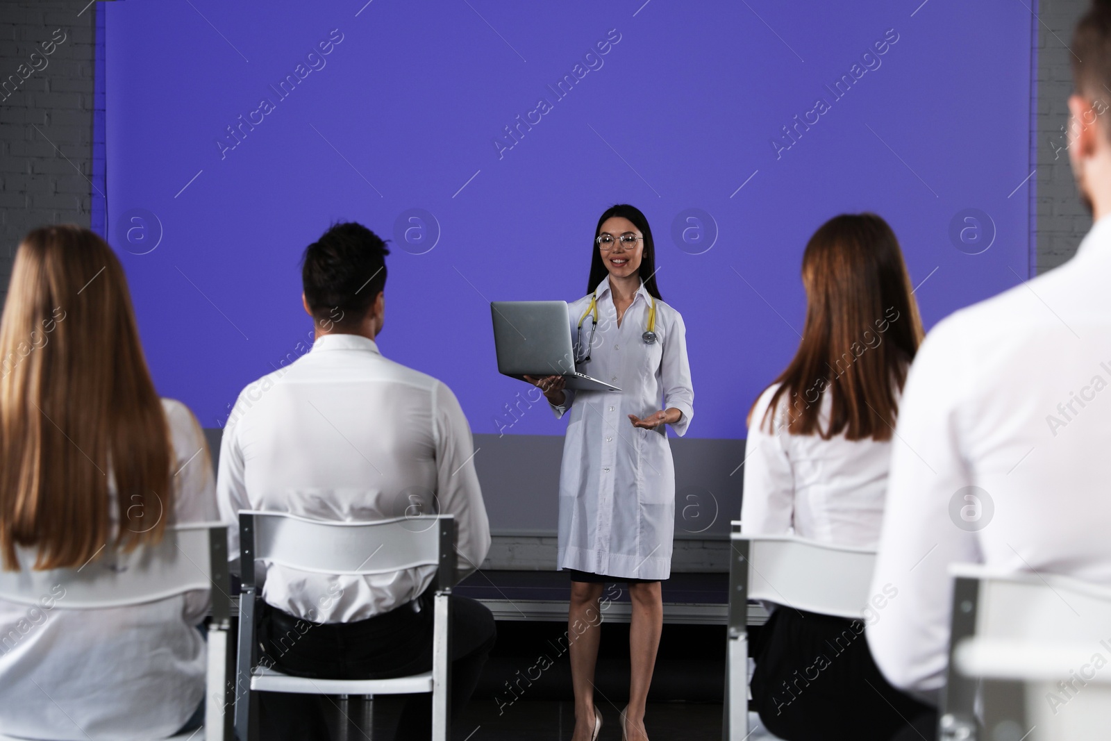Female doctor with laptop giving lecture in conference room with projection screen Photo of Female doctor with laptop giving lecture in conference room with projection screen