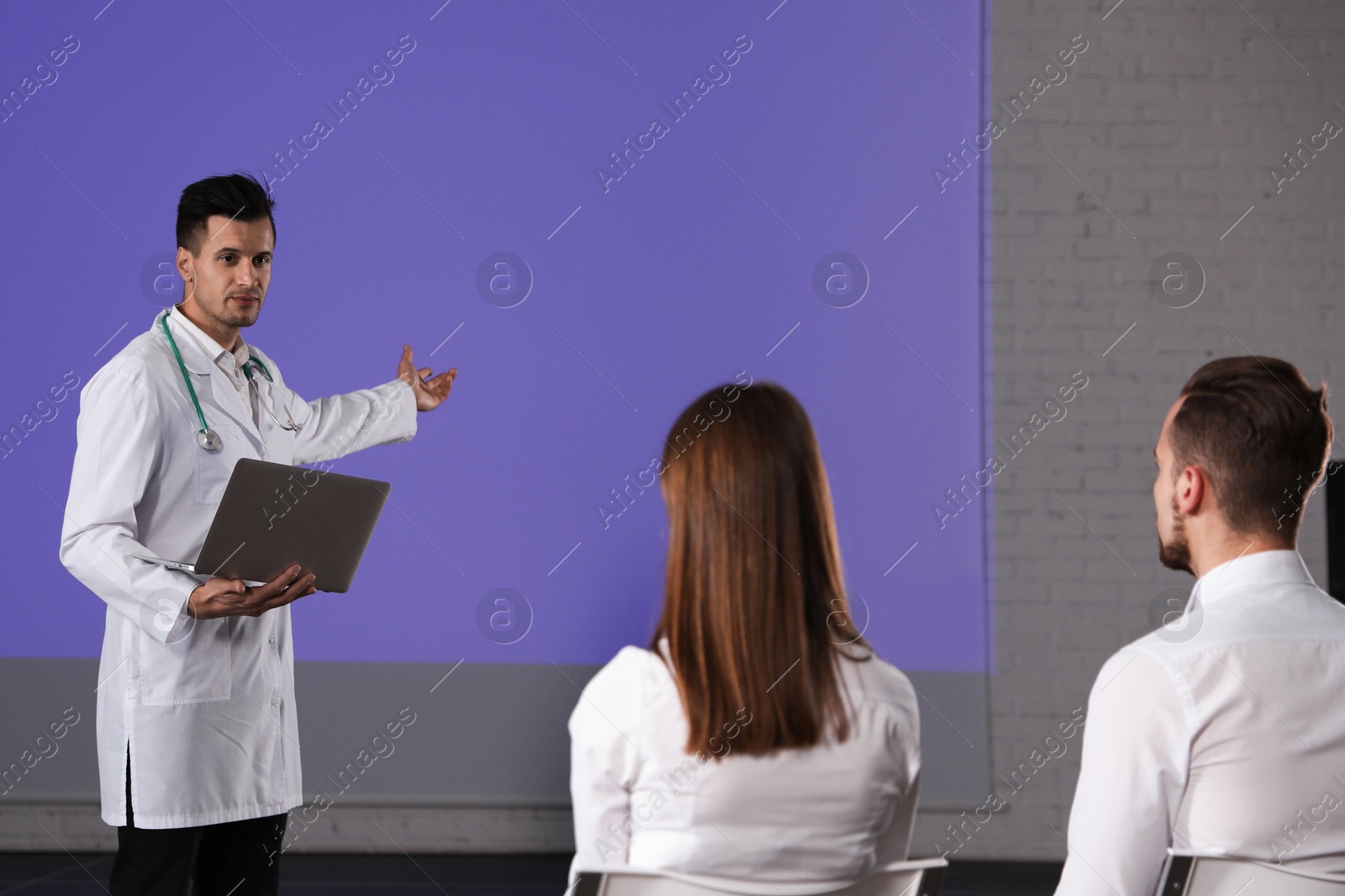 Male doctor with laptop giving lecture in conference room with projection screen Photo of Male doctor with laptop giving lecture in conference room with projection screen
