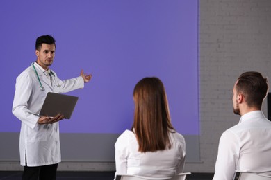 Photo of Male doctor with laptop giving lecture in conference room with projection screen