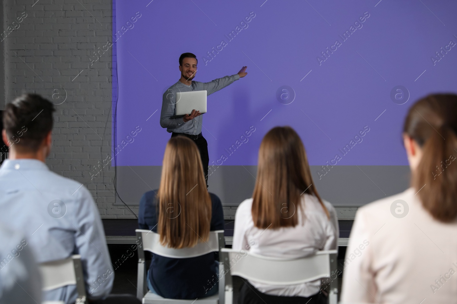 Male business trainer with laptop giving lecture in conference room with projection screen Photo of Male business trainer with laptop giving lecture in conference room with projection screen