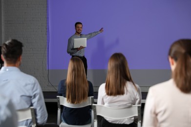 Photo of Male business trainer with laptop giving lecture in conference room with projection screen