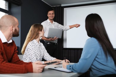 Photo of Business people listening to speaker in conference room with video projection screen