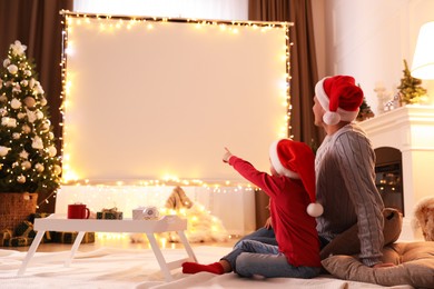 Photo of Father and daughter watching movie using video projector at home. Cozy Christmas atmosphere