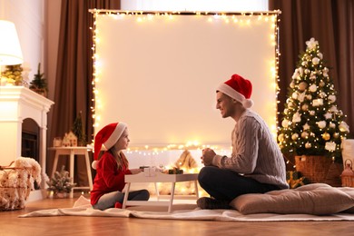 Photo of Father and daughter near video projector screen at home. Cozy Christmas atmosphere