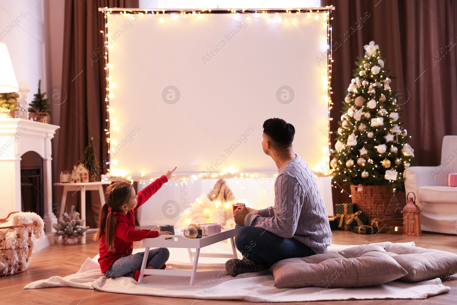 Father and daughter watching movie using video projector at home. Cozy Christmas atmosphere Photo of Father and daughter watching movie using video projector at home. Cozy Christmas atmosphere