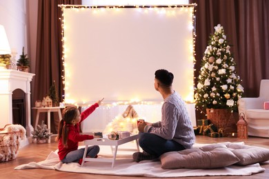 Photo of Father and daughter watching movie using video projector at home. Cozy Christmas atmosphere