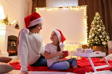 Photo of Mother and daughter near video projector screen at home. Cozy Christmas atmosphere