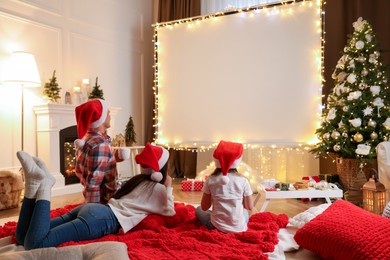 Photo of Family watching movie using video projector at home. Cozy Christmas atmosphere