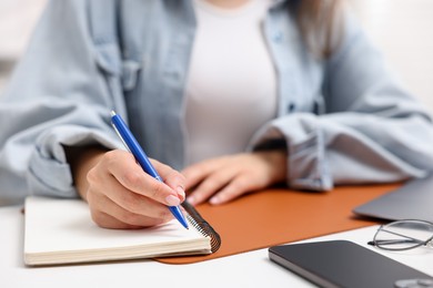 Photo of Woman writing in planner at white desk indoors, closeup