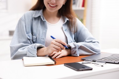 Photo of Woman with planner, smartphone and laptop at white desk indoors, closeup