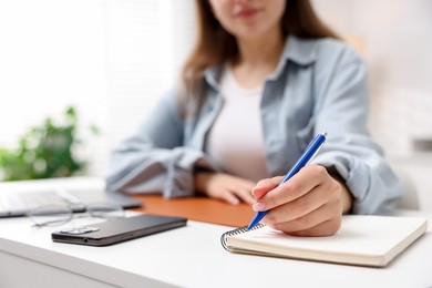 Photo of Woman with planner and smartphone at white desk indoors, closeup