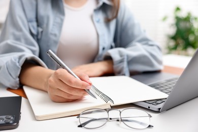 Photo of Woman with planner and laptop at white desk indoors, closeup