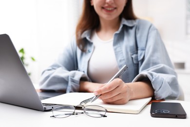 Photo of Woman with planner and laptop at white desk indoors, closeup