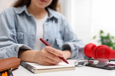 Photo of Woman writing in planner at white desk indoors, closeup
