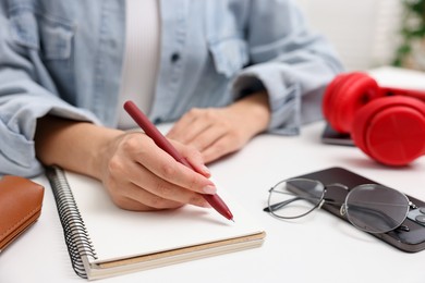Photo of Woman writing in planner at white desk indoors, closeup