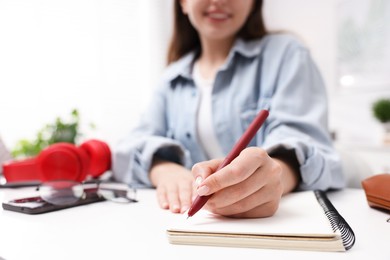 Photo of Woman writing in planner at white desk indoors, closeup